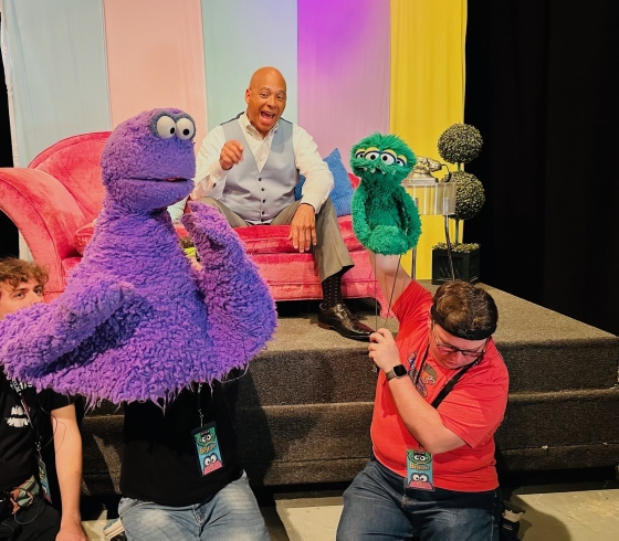 Actor for Be Happy in a scene with puppets and puppeteers